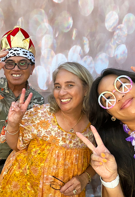 Family of three making silly faces with photo booth props at an event in Long Beach, California
