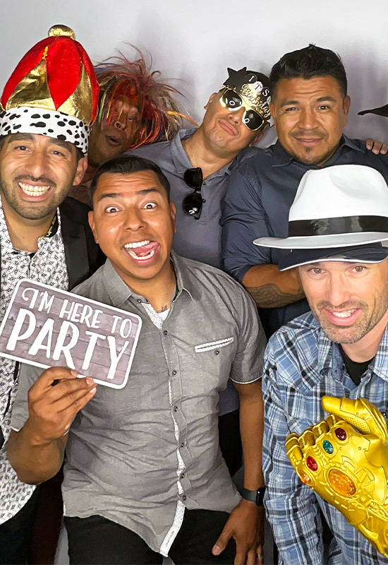 Group of grown men wearing silly hats and props while posing in a photo booth and making funny faces