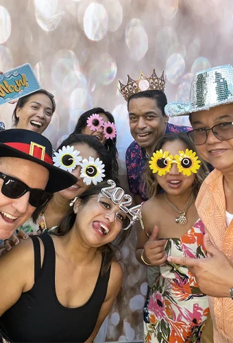 group of adults wearing hawaiian outfits and fun sunglasses at photo booth in Manhattan Beach California