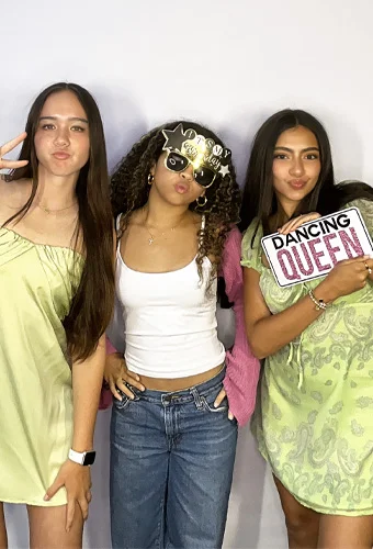 teen girls using photo booth at sweet 16 in Santa Monica California wearing birthday sunglasses and props