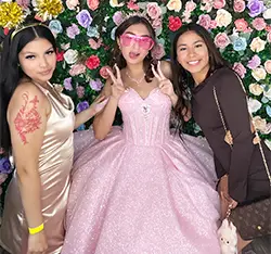 Three girls posing at a quinceañera photo booth with a floral backdrop in Torrance, CA